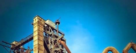 Vista externa de uma usina industrial com torres, tubulações e céu azul.