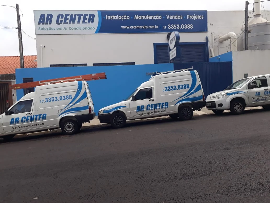 Vans brancas da AR CENTER estacionadas lado a lado, com a marca e o telefone impressos na lateral.
